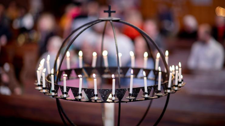 En lysglobe fylt av lys i en kirke. De mange små lysene står i fokus, mens man kan skimte at kirken er full av mennesker bak.