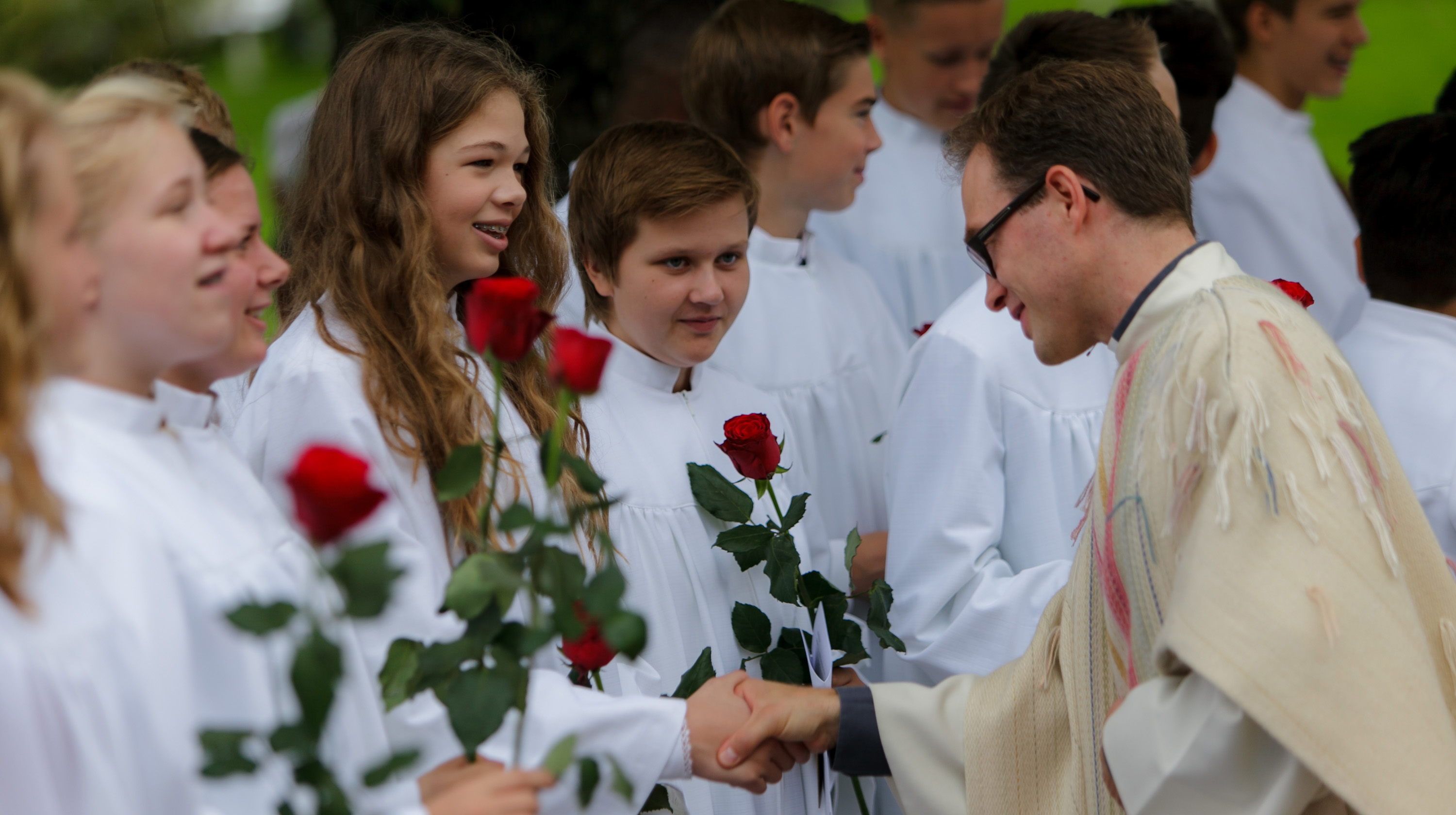 Mange konfirmanter står på en rekke. En prest håndhilser og gir roser til konfirmantene.